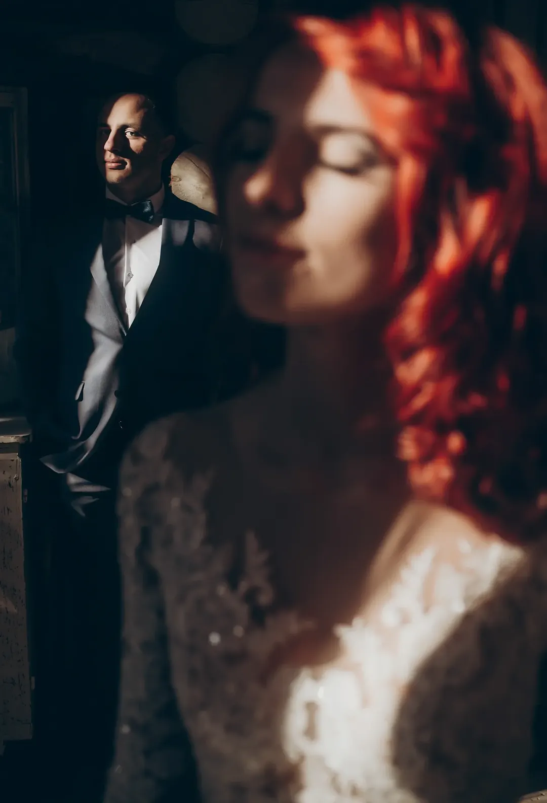 A red-haired woman in the foreground and a man in an elegant suit in the background