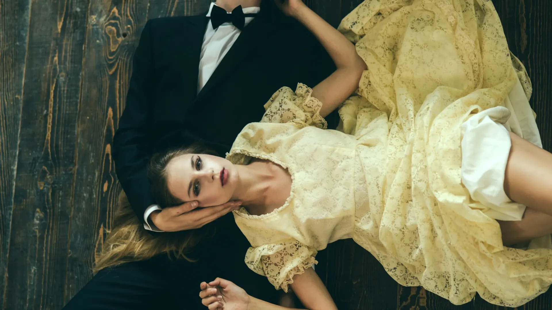Ein Mann im Smoking und eine Frau in einem hellen Kleid liegen auf einem Holzboden