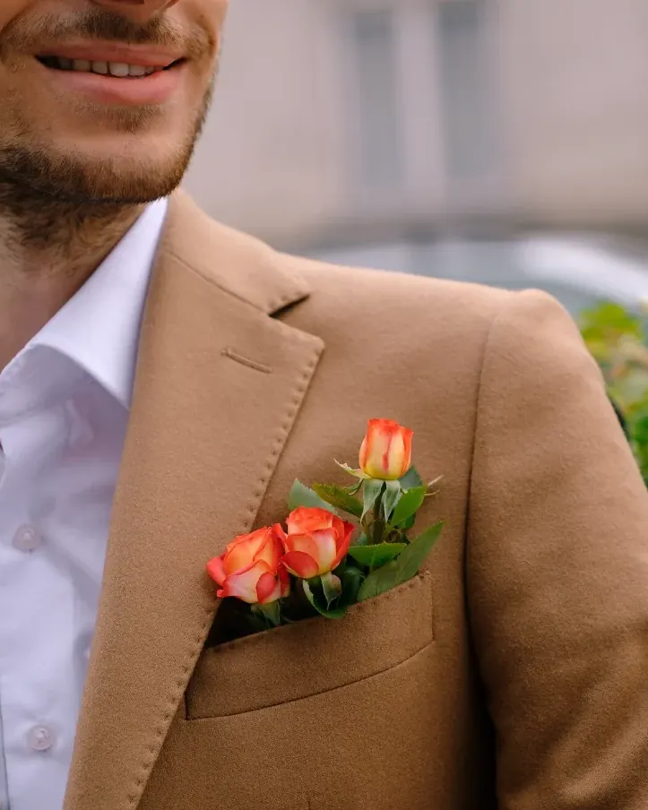 Un hombre sonriente con chaqueta color camel y un ramillete de flores en el bolsillo del pecho