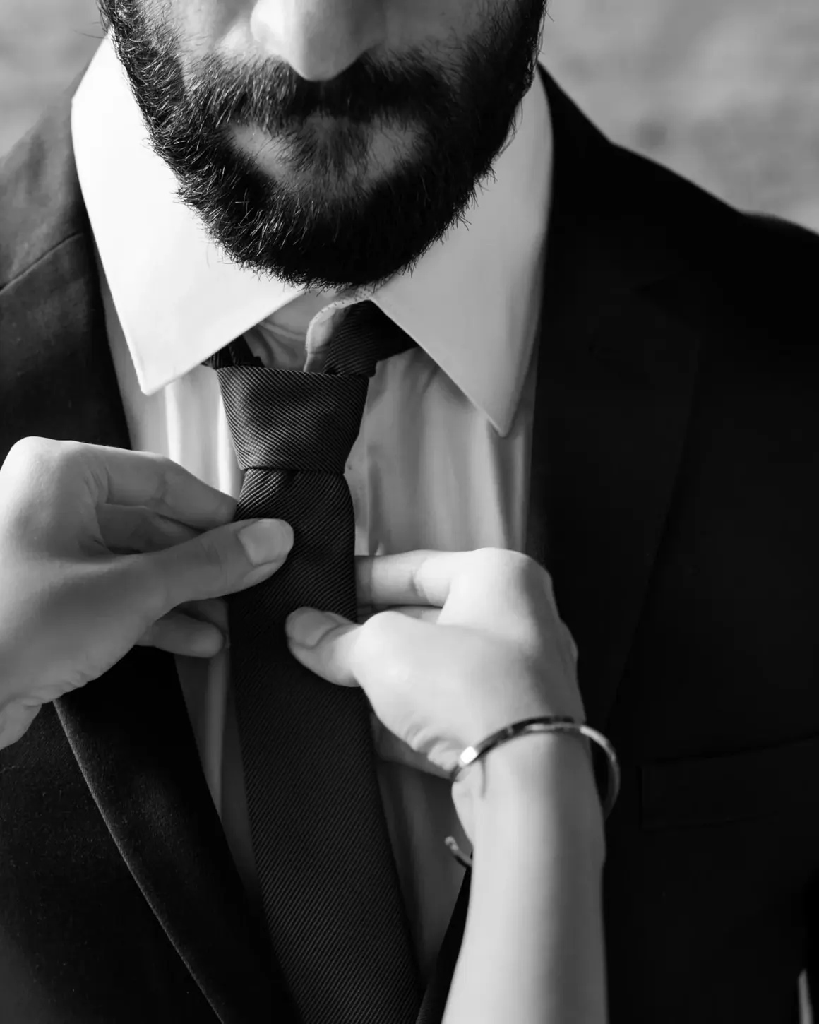 Unas manos femeninas ajustan la corbata de un hombre con traje oscuro